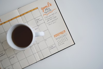 計画表の上にコーヒーの入ったコーヒーカップが乗っている画像