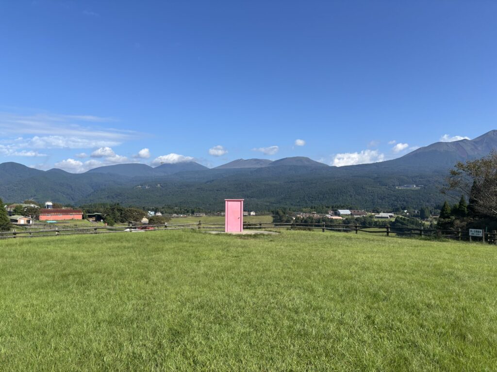 背景に霧島連山を臨み、中央に高千穂牧場「どこどでんドア」（ピンク）の写った写真