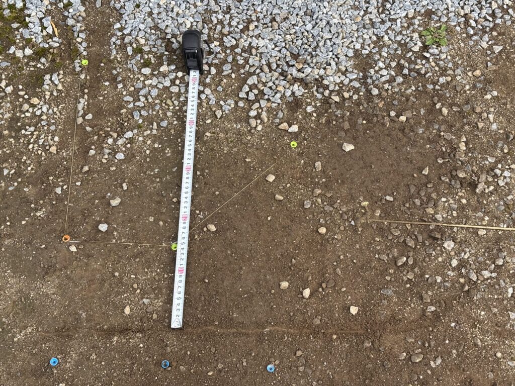 ホームベースとバッターボックスの位置にゴルフのロングティーを埋め込んで、足場を固定した写真：メジャーでベースから15cmを計測しているメジャーも写っている