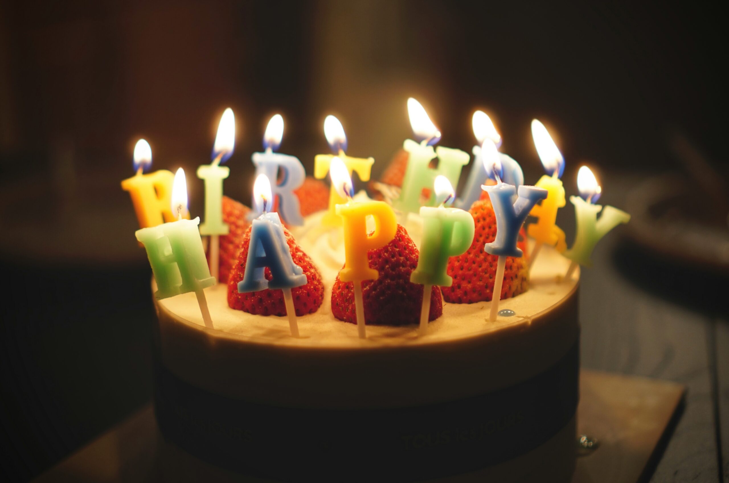 誕生日のケーキの上にHAPPY BIRTHDAYの文字型の火の付いたろうそくの画像